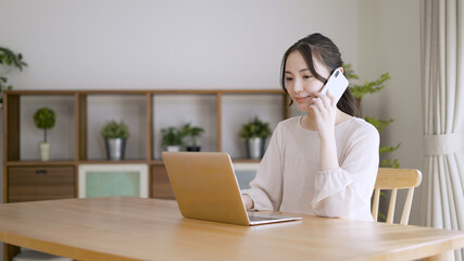 電話をしながらラップトップを使う若い女性