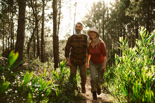 caucasian happy senior couple hiking through forest on sunny day