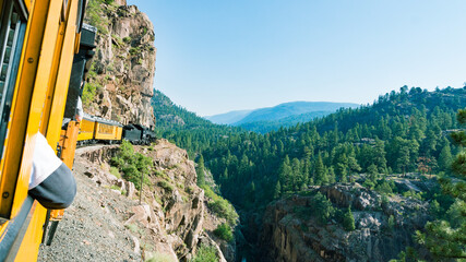 Old-fashioned train of the touristic route from Durango to Silverton (USA), running close to a cliff. Green valley on the right. - obrazy, fototapety, plakaty