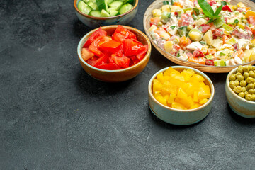 side close view of bowl of vegetable salad with bowls of vegetables on side on dark green background