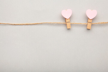 Two pink clothespins hearts hanging on rope on grey background.