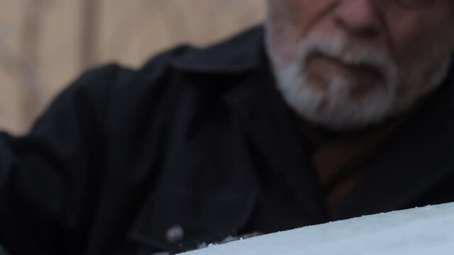 Hasty man hand holds black yellow ice scraper and cleans electric car windshield on cold winter day slow motion