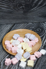 Marshmallows on a wooden plate. A little scattered nearby. On black pine planks.