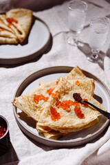 Traditional Russian crepes or pancakes with red caviar on gray plates and glasses of ice vodka over greige linen tablecloth. Pancake week or Shrovetide