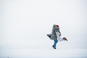 On a white background of a snowy plain, a couple of lovers run and hug during a date.