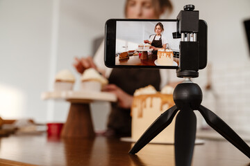 Camera footage of focused baker woman making cakes with cream in kitchen