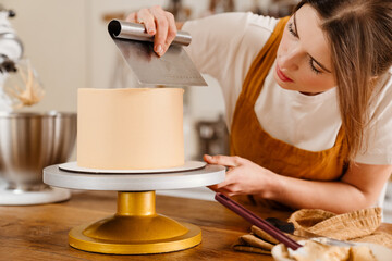 Beautiful concentrated pastry chef woman making cake with cream