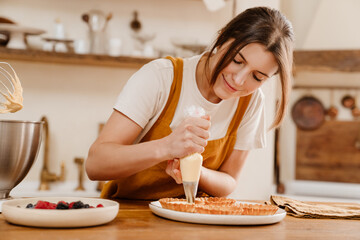 Beautiful happy pastry chef woman smiling while making tarts with cream