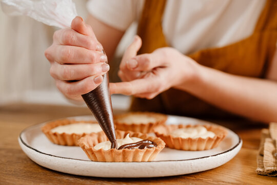 Caucasian pastry chef woman making tarts with cream at cozy kitchen