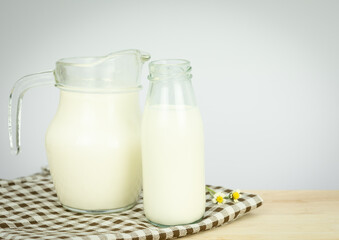  A jug and bottle of milk glass on a wooden table on background. Raw milk is high in calcium and protein to drink for all ages. Milk consumption nutritious and healthy dairy products concept..