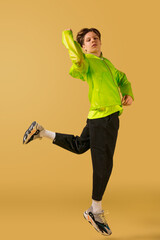 Fototapeta na wymiar Jump. Old-school fashioned young man dancing isolated on yellow studio background. Artist fashion, motion and action concept, youth culture, fashion returning. Young caucasian curly boy.