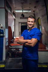 Pleased young man in a medical uniform, ambulance car in the background.