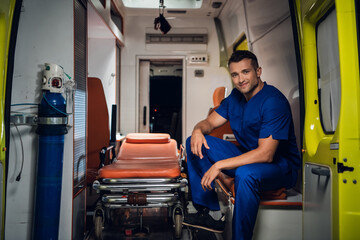 Smiling paramedic in a blue uniform sitting in the back of an ambulance car.