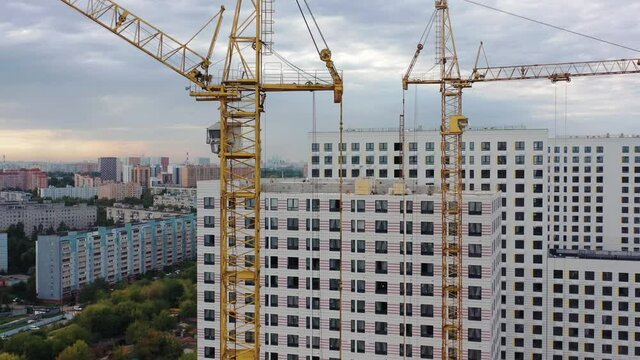 Residential complex with high-rise apartment houses under construction, aerial drone zoom in shot. Two building cranes, new apartment under construction, grey sky