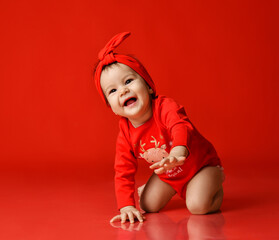 Happy laughing infant baby girl toddler in red bodysuit at Christmas Eve New Year stands on all fours crawling to camera over red background. Translation: Happy New Year