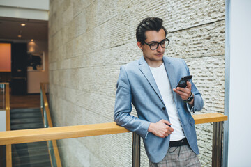 Trendy male manager surfing internet on smartphone during break