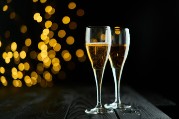 Two glasses of sparkling wine or champagne to celebrate New Year, Merry Christmas or Anniversary with a bokeh effect background. The yellow of the wine and lights stand out against a dark background.