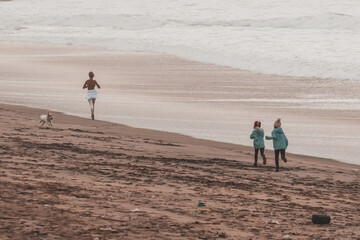 Fototapeta na wymiar Girl running on the beach by the sea with two kids