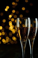 Two glasses of sparkling wine or champagne to celebrate New Year, Merry Christmas or Anniversary with a bokeh effect background. The yellow of the wine and lights stand out against a dark background.