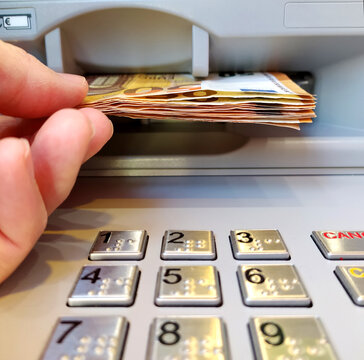 A person taking out cash in fifty euro bills from a bank cash machine