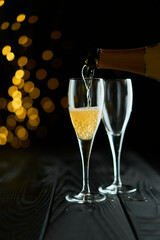 Two glasses of sparkling wine or champagne to celebrate New Year, Merry Christmas or Anniversary with a bokeh effect background. The yellow of the wine and lights stand out against a dark background.