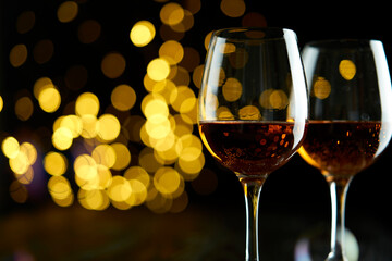 Two glasses of sparkling wine or champagne to celebrate New Year, Merry Christmas or Anniversary with a bokeh effect background. The yellow of the wine and lights stand out against a dark background.
