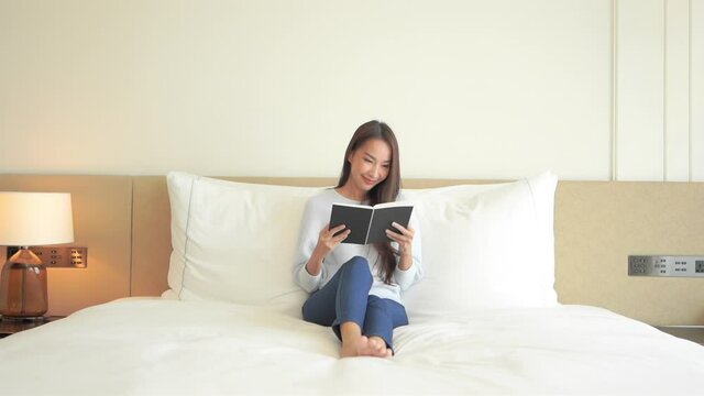 A young attractive woman enjoys some quiet time while sitting propped up in her hotel suite bed reading a book.