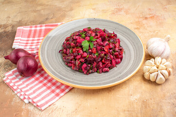 top view of plate of a red salad with greens on it on a wooden backgorund with vegetables at the side with checked napkin