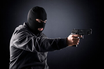 Criminal wearing black balaclava and hoodie with a gun in the dark