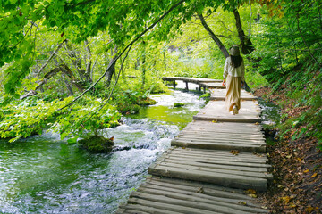 Fototapeta premium Young woman traveler walking on wooden path trail in Plitvice Lakes National Park, UNESCO natural world heritage and famous travel destination of Croatia