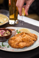 hand squeezing lemon Weiner Schnitzel with Potatoes and sauce on the table at restaurant
