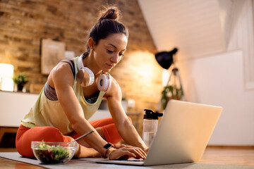 Athletic woman tying on laptop while sitting on the floor at home.