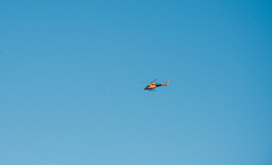 Helicóptero amarillo naranja volando con fondo de cielo azul sin nubes