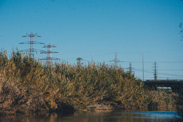 Torres eléctricas de fondo en un río con puente de fondo. Contraste urbano y naturaleza