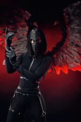 a woman wearing a plague doctor mask with leather straps and black wings on a dark red background