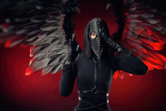 a woman wearing a plague doctor mask with leather straps and black wings on a dark red background