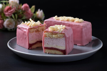 Sliced mousse desserts with almond biscuit, strawberry coolie and strawberry mousse covered gourmet pink chocolate glaze on black background. Closeup
