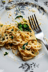 Spaghetti in creamy spinach sauce with cheese, on a messy floral plate with silver fork, half eaten