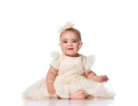 Happy child girl in a festive dress and headband sitting on the floor. Toddler toddler looking at camera studio portrait shot on white background. Childrens fashion and beauty