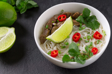 Pho Bo - Vietnamese fresh rice noodle soup with beef, herbs, lime and chili. Vietnamese national dish.