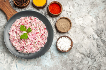 Half shot of tasty chicken salad with mayonnaise and beet served with green on brown wooden cutting board and different spices on ice background