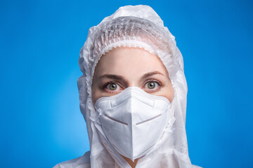 Close-up portrait of female doctor wearing protective suit to fight coronavirus pandemic covid-2019. Tired doctor on blue background