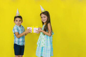 A little boy gives a gift to a girl on a bright yellow background.birthday of a little girl.