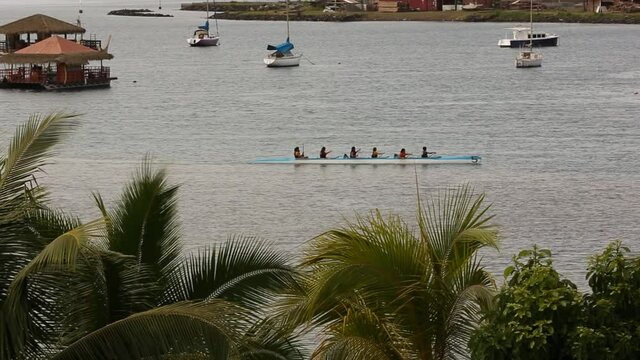 Group of people canoeing on the tahitian sea with yachts in the background.
