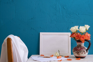 a bouquet of roses in an old vase, a set for writing, a white frame for a photo on a blue background