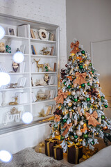 Christmas tree with shyning garland decorated in gold and brown decor. Cozy home interior. New year decoration. White room with large bookshelves.