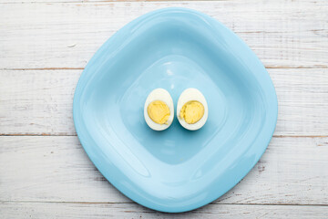 Boiled egg cut into two halves on a blue plate on a white wooden background.