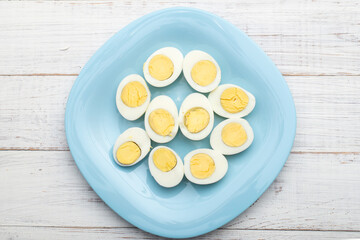 Boiled eggs cut into two halves on a blue plate on a white wooden background.