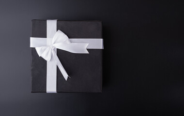 black gift box with white ribbon on black background flat lay top shot