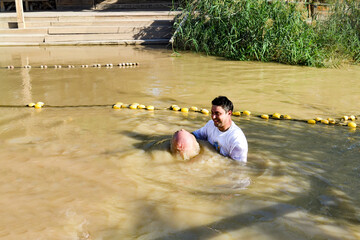 a man toes underwater at his baptism in the Jordan River. The priest holds his hands